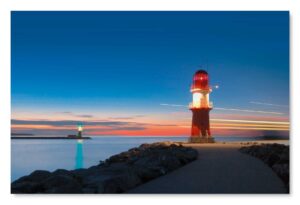 Ein Küstenland - Molenfeuer in Warnemünde an einem felsigen Küstenlandufer in der Abenddämmerung.