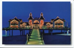 Ein beleuchtetes Gebäude mit einer Rügen - Meine Insel - Seebrücke Sellin im Hintergrund in Sellin auf der Insel Rügen.